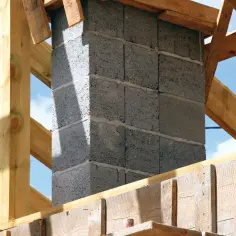 Budowa komina z pustaków betonowych, widoczne drewniane elementy konstrukcji dachu i szalunek. Zbrojenie pod komin jest kluczowe dla jego stabilności.