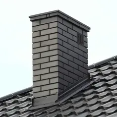 Nowoczesny komin z ciemnej cegły, wykończony metalową obróbką, idealnie komponuje się z czarnym dachem.