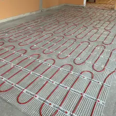 Czerwone rury ogrzewania podłogowego ułożone na siatce na betonowym podłożu.