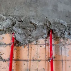 Czerwone rury ogrzewania podłogowego pod mokrą wylewką betonową.