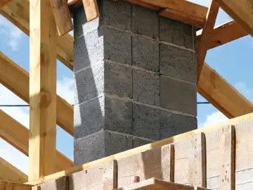 Budowa komina z pustaków betonowych, widoczne drewniane elementy konstrukcji dachu i szalunek. Zbrojenie pod komin jest kluczowe dla jego stabilności.